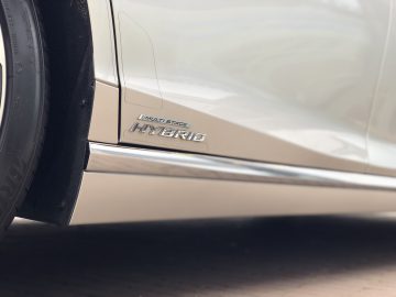 Close-up van de onderkant van een Lexus LS met het 'Multi Stage Hybrid'-embleem boven een chromen strip bij de deurdrempel.