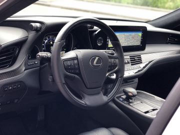 Binnenaanzicht van een Lexus LS met het stuur, het dashboard met digitale instrumenten, het bedieningspaneel en het navigatiescherm.