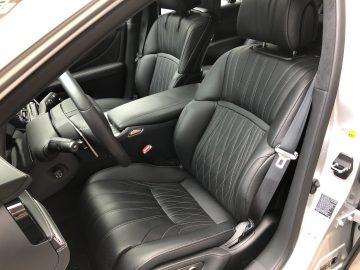 Het interieur van de Lexus LS is voorzien van zwart lederen stoelen en een modern dashboard met een stuur aan de linkerkant en een middenconsole in het midden. Het bestuurdersportier staat open en laat het elegante ontwerp zien.