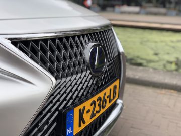 Close-up van de grille van een Lexus LS met een Europees kenteken met de tekst K-236-LB, geparkeerd nabij een watermassa.