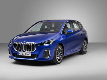 Een blauwe BMW 2 Serie Active Tourer hatchback staat geparkeerd in een studio met een grijze achtergrond, met een voor- en zijaanzicht.