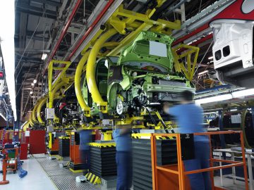 Werknemers die auto's assembleren op een geautomatiseerde productielijn met verschillende auto-onderdelen en machines in een fabrieksomgeving, waardoor de benodigde nieuwe auto voor enthousiaste kopers efficiënt wordt verminderd.