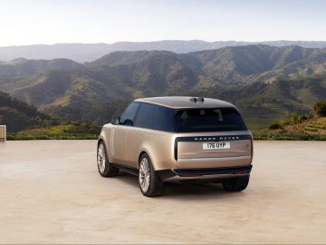Een slanke Range Rover SUV staat geparkeerd op een betonnen ondergrond, perfect omlijst door een adembenemend berglandschap onder een heldere hemel.