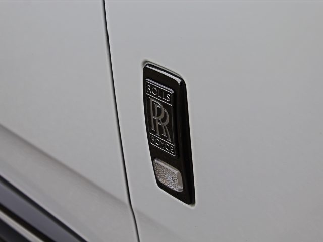 Close-up van een Rolls-Royce-embleem op de witte buitenkant van een Rolls-Royce Cullinan Black Badge-voertuig.