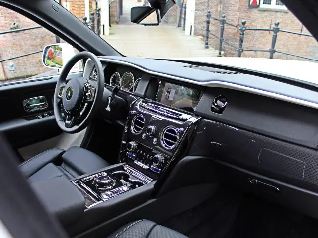 Binnenaanzicht van een Rolls-Royce Cullinan Black Badge met een luxe auto met een goed uitgerust dashboard, een stuurwiel versierd met het iconische logo, meerdere bedieningspanelen en een groot touchscreen.