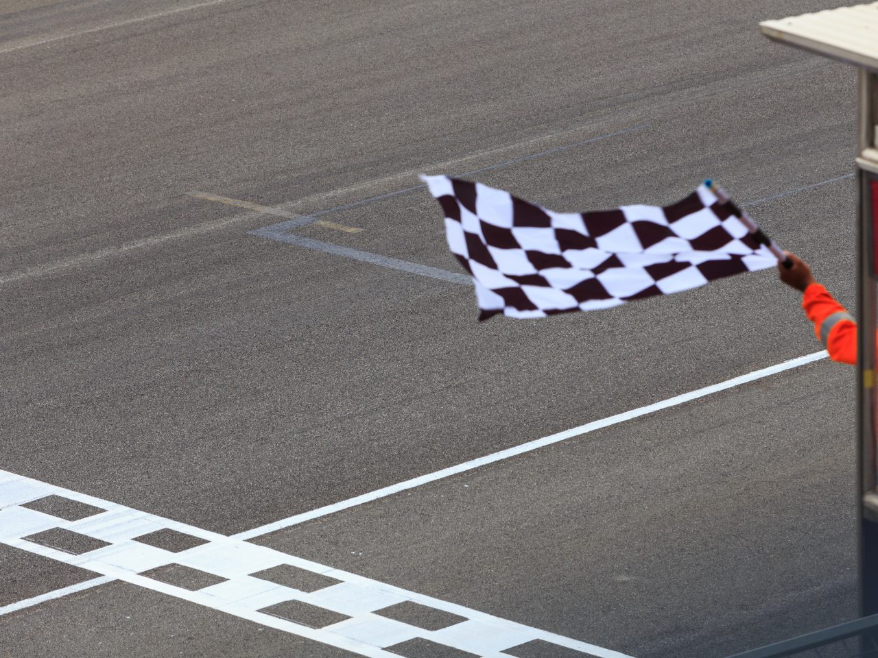 Op een racebaan wordt met een geblokte vlag gezwaaid terwijl een sportofficial het einde van een race aangeeft. Dit markeert het moment waarop fans hun online weddenschap plaatsen om hun strategieën te vieren of te heroverwegen.