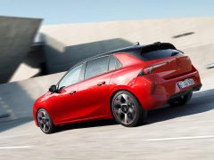Een rode, moderne Opel Astra hatchback rijdt op een weg vlakbij een betonconstructie.