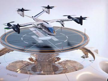 Een conceptafbeelding van een vliegende auto met het merk Supernal Hyundai die landt op een futuristisch rond landingsplatform. Het voertuig heeft vier sets propellers en lijkt zich in een stedelijke omgeving te bevinden.