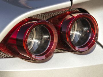 Close-up van de achterlichten van een auto, met twee ronde rode lenzen tegen een zilverkleurige metalen behuizing, bijna een uitdagende quiz voor je ogen.