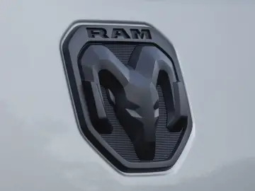 Close-up van een zwart-zilveren RAM 1500-logobadge op een lichtgekleurd voertuig.