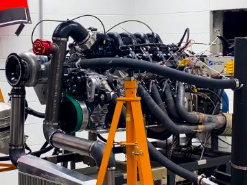 Een complexe Ford-motor met turbocompressor staat op een testopstelling in een laboratorium gemonteerd, waaraan verschillende slangen, draden en meetinstrumenten zijn aangesloten.