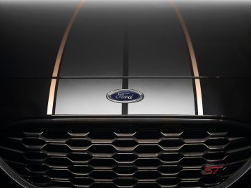 Close-up van de grille en motorkap van een Ford Puma ST Gold Edition, met het iconische Ford-embleem, opvallende zwart-witte strepen en een opvallende 'ST'-badge.