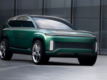 Een slanke, groene Hyundai SEVEN concept-SUV met futuristische designkenmerken, waaronder LED-verlichting en een gestroomlijnde carrosserie, geparkeerd voor een modern glazen gebouw.