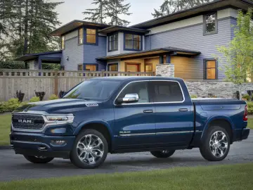 Een blauwe pick-up RAM 1500 staat geparkeerd voor een modern huis van twee verdiepingen met een goed onderhouden tuin en bomen.