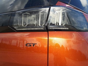 Close-up van de achterlichten en het "GT" -embleem op een oranje Peugeot 5008.