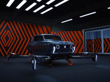 Een zwart drone-achtig voertuig met een Renault 4-autochassis wordt tentoongesteld in een kamer met zwarte en oranje geometrische muurpatronen en bovenlichten.