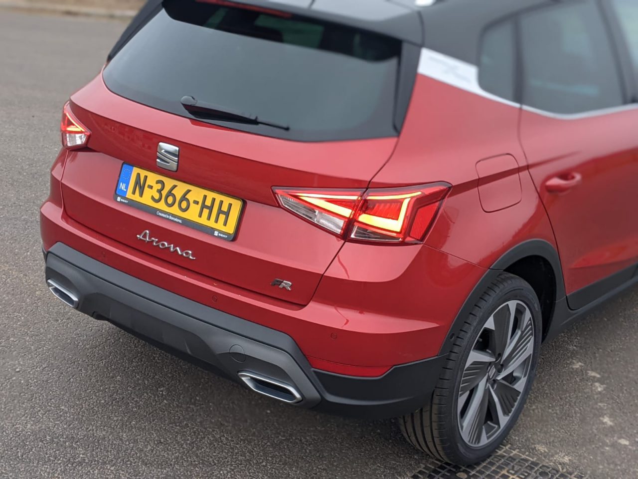 Rode SEAT Arona met Nederlands kenteken N-366-HH, gezien vanaf de achterkant. De auto is voorzien van opvallende achterlichten en dubbele uitlaten en staat geparkeerd op een verharde ondergrond. Deze SEAT Arona-recensie benadrukt het strakke ontwerp en de indrukwekkende details aan de achterkant.
