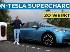 Er staat een persoon naast een blauwe elektrische auto geparkeerd bij een Tesla Supercharger-station, met daarboven de tekst “Non-Tesla Superchargen Zo Werkt Het”.