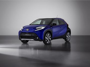 Een blauwe compacte crossover Toyota Aygo X wordt tentoongesteld in een goed verlichte, minimalistische studioomgeving, wat het strakke ontwerp benadrukt.