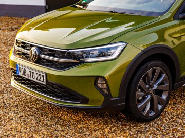 Een close-up van een groene Volkswagen Taigo SUV geparkeerd op een grindoppervlak, met de grille, koplampen en kentekenplaat.