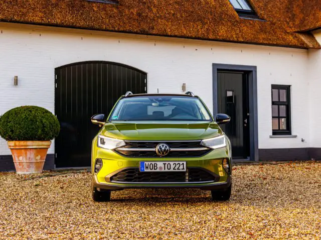 Vooraanzicht van een groene Volkswagen Taigo SUV geparkeerd voor een wit huis met zwarte deuren en ramen.