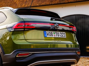 De achterkant van een groene Volkswagen Taigo SUV wordt getoond, waarbij de achterlichten, kentekenplaat en modelnaam tegen een vage garagedeurachtergrond worden benadrukt.