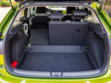 De achterklep van de groene Volkswagen Taigo onthult zijn ruime bagageruimte, met de achterbank gedeeltelijk neergeklapt.