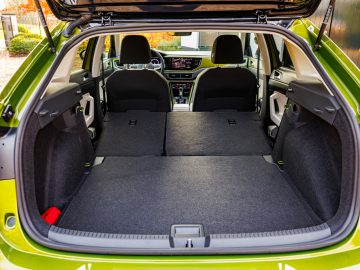 Een zicht op de ruime laadruimte van een groene Volkswagen Taigo SUV met neergeklapte stoelen om een vlak en verlengd laadoppervlak te creëren. Het interieur en het dashboard van het voertuig zijn ook gedeeltelijk zichtbaar.