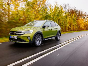 Een groene Volkswagen Taigo SUV rijdt op een natte weg omringd door herfstkleurige bomen.