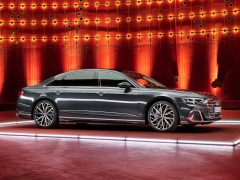 Een strakke zwarte Audi A8 sedan wordt tentoongesteld op een verlicht platform tegen een achtergrond van rode en oranje lichten.