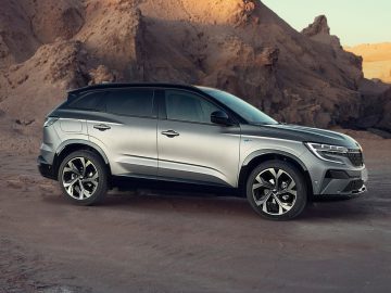 Een zilveren SUV, gekroond tot Auto van het jaar 2023, staat geparkeerd op een desolaat rotsachtig landschap waar een mix van zonlicht en schaduwen de kenmerken ervan benadrukt.