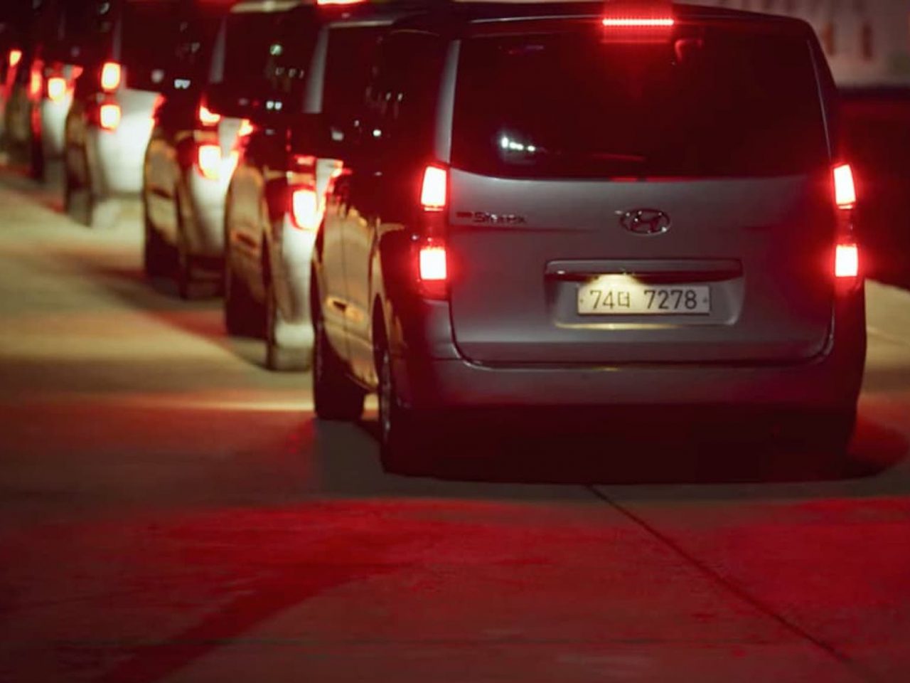 Verschillende auto's staan 's nachts in de rij, terwijl hun remlichten het tafereel verlichten. De laatste auto in de rij is een zilveren Toyota, met een Zuid-Koreaans kenteken, dat doet denken aan een spannend moment uit Squid Game.