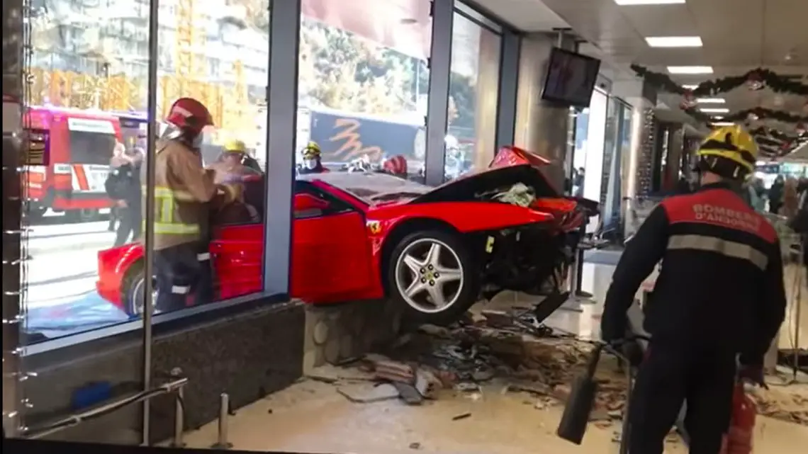 Een rode Ferrari botste tegen het glazen raam van een gebouw. Hulpverleners in uniform doen onderzoek ter plaatse. Er ligt vuil op de vloer in het gebouw.