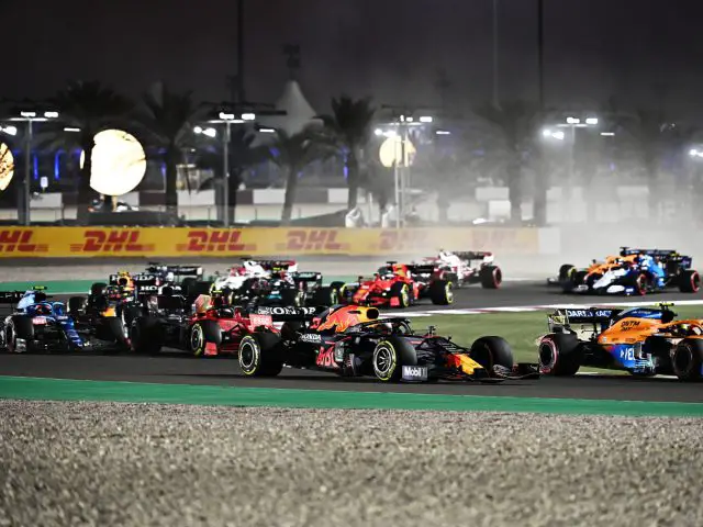 Raceauto's strijden 's nachts op een circuit, met zichtbare bandensporen en lichte waas. Palmbomen en lichtreclames bevinden zich op de achtergrond en vangen de opwindende essentie van Formule 1 2022 op.