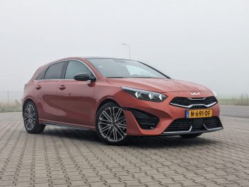 Een rode Kia Ceed hatchback met kenteken N-691-DF staat geparkeerd op een verhard oppervlak, gezien vanuit de hoek linksvoor onder een bewolkte hemel.