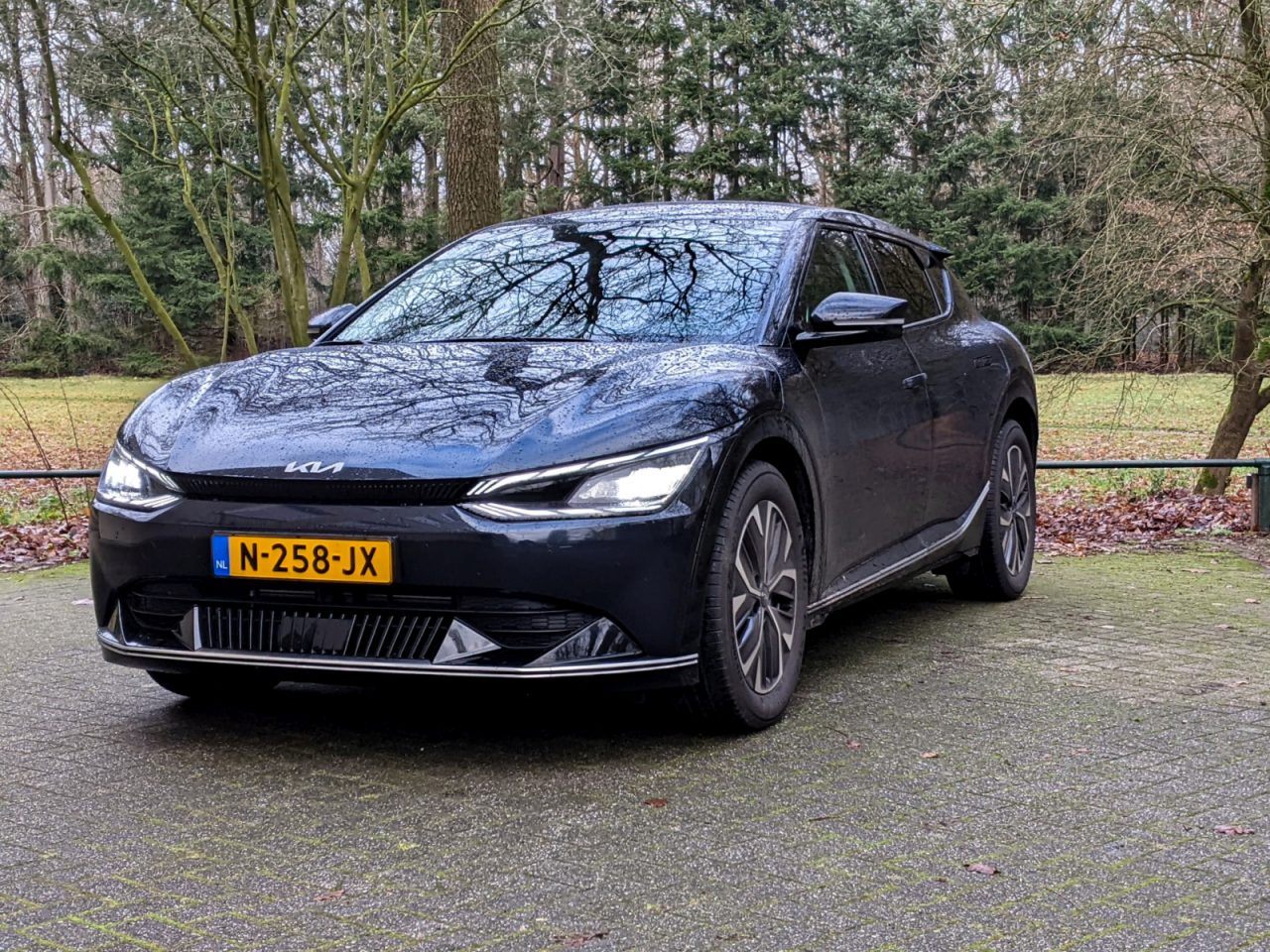 Een strakke zwarte Kia EV6 met Nederlands kenteken N-258-JX staat geparkeerd op een verharde ondergrond in een serene bosrijke omgeving.