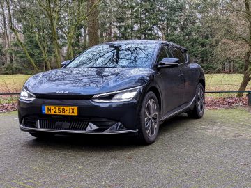 Een strakke zwarte Kia EV6 met Nederlands kenteken N-258-JX staat geparkeerd op een verharde ondergrond in een serene bosrijke omgeving.