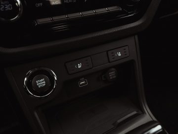 Close-up van de middenconsole van een SsangYong Korando e-Motion met een Start/Stop-motorknop, klimaatregelingsknoppen, stoelverwarmingsknoppen, een USB-poort, 12V-stopcontact en een opbergvak.