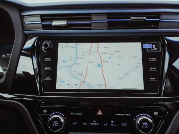 Dashboardweergave van een SsangYong Korando e-Motion met een navigatiesysteem op het middenscherm met een kaart met routes, naast de fysieke klimaatknoppen eronder.