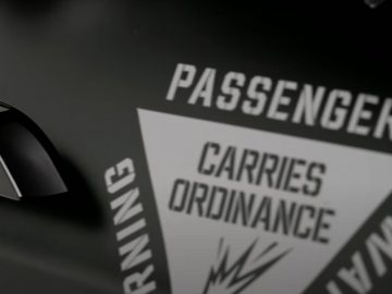 Close-up van een gedeelte van een Tesla Model S geruite deur met de tekst "Passenger Carries Ordnance Warning" in een driehoekig waarschuwingsbord.