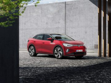 Een rode Volkswagen ID.5 elektrische SUV staat geparkeerd op een verhard oppervlak nabij een moderne betonnen muur en houten balken.