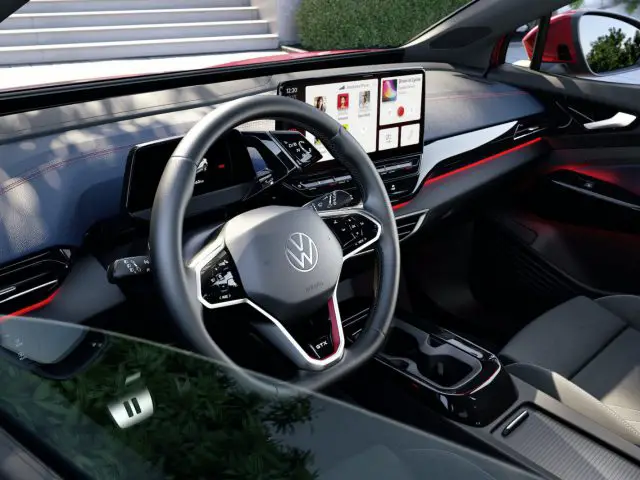 Interieur van een moderne Volkswagen ID.5 met een VW-badge op het stuur, een digitaal dashboarddisplay, touchscreen-infotainment en zwarte bekleding met rode stiksels.