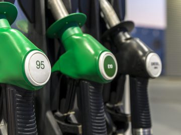 Close-up van drie brandstofsproeiers bij een benzinestation, met het opschrift "95", "E10" en "Diesel." De groene benzinesproeiers contrasteren scherp met hun zwarte handvatten.