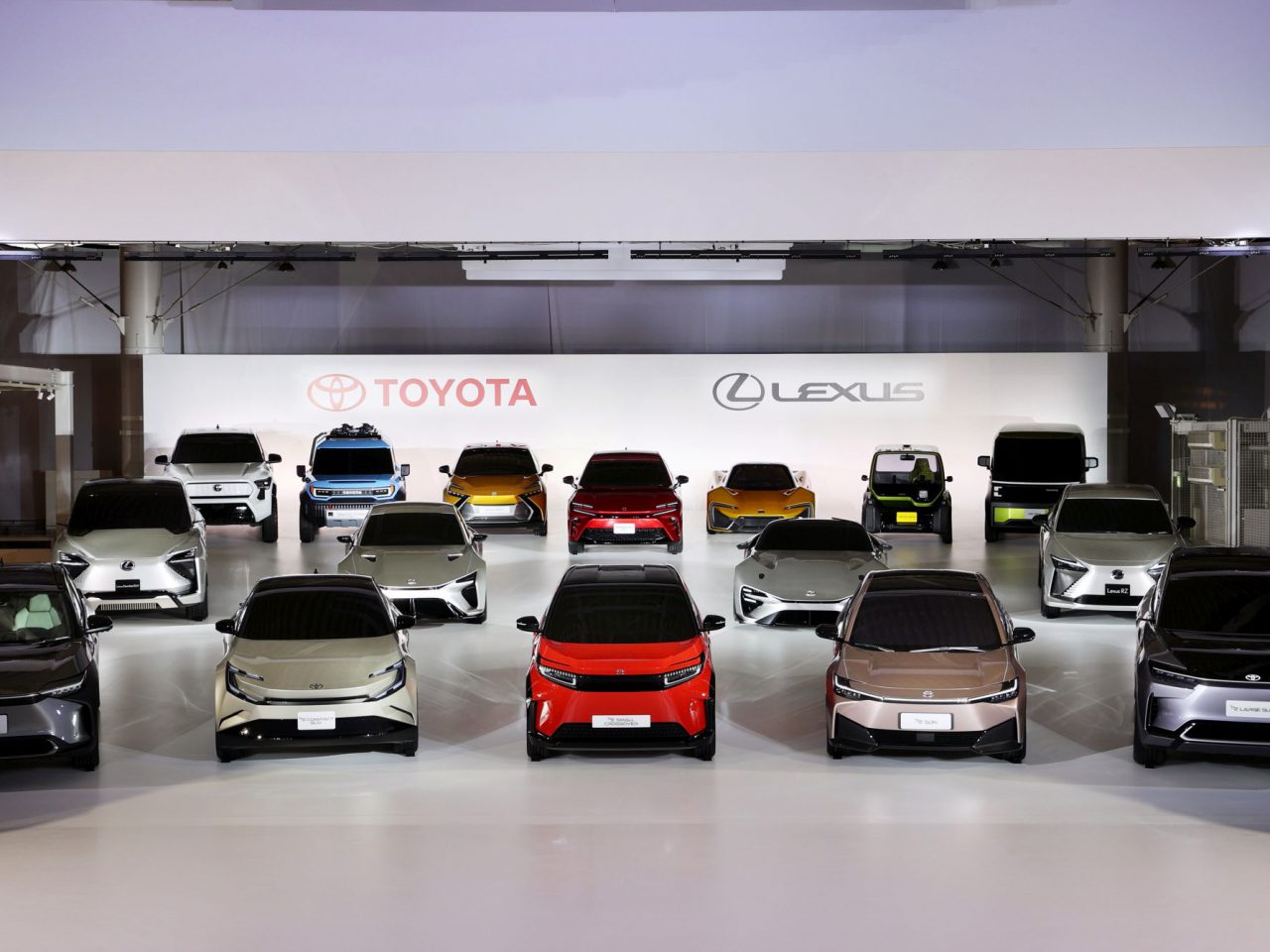 Een showroom met een reeks Toyota- en Lexus-voertuigen, waaronder de nieuwste Toyota BEV-modellen in verschillende kleuren, gerangschikt in rijen met merklogo's zichtbaar op de achtergrond.