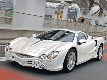 Een witte sportwagen rijdt over een stadsweg met verhoogde wegen en gebouwen op de achtergrond, wat scherp contrasteert met enkele van de lelijkste auto's die vlakbij geparkeerd staan.