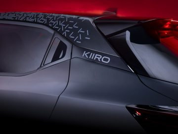 Close-up van de achterkant van een auto met een 'KIIRU'-badge, geometrische patronen bij de achterruit en gloeiende rode achterlichten tegen een donkerrode achtergrond, die doet denken aan het opvallende ontwerp van de Nissan Juke.