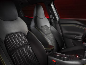 Binnenaanzicht van een Nissan Juke met twee zwarte voorstoelen met gele stiksels, een middenarmsteun en een console met bekerhouders.