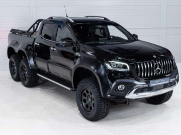 Een zwarte, zeswielige Mercedes-Benz X350d pick-up met zes wielen staat geparkeerd in een witte binnenruimte en laat het robuuste ontwerp en de aangepaste aanpassingen zien.