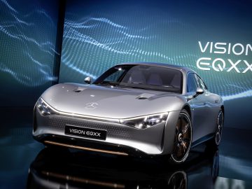 Een zilveren Mercedes-Benz Vision EQXX-conceptauto tentoongesteld voor een digitale achtergrond met de tekst 'VISION EQXX', die de innovatie en elegantie laat zien die synoniem is aan het merk Mercedes-Benz.