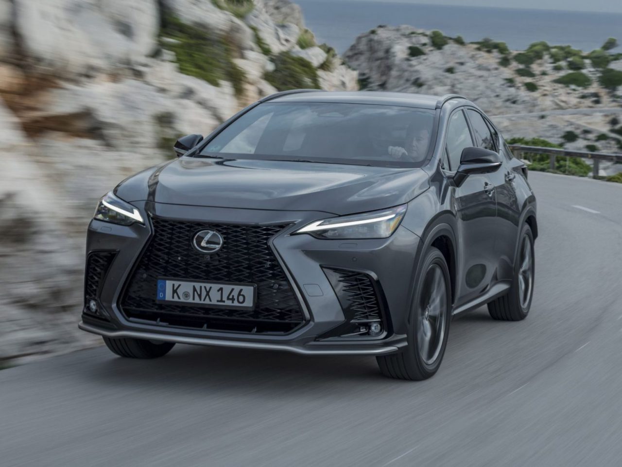 Een zilveren Lexus NX SUV, een betrouwbare auto, rijdt op een bochtige weg door een rotsachtig kustlandschap.